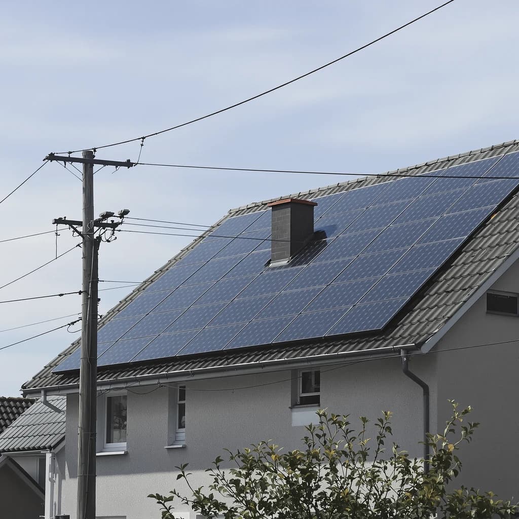 Solarmodule auf dem Satteldach eines Wohnhauses, davor ein Holzmast mit Freileitung.
