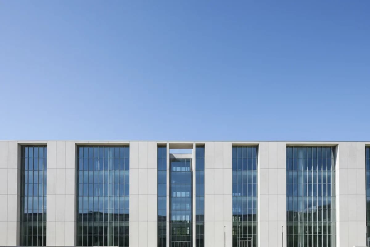 Fassade eines modernen Verwaltungsgebäudes mit hohen, schmalen Fensterachsen vor blauem Himmel.